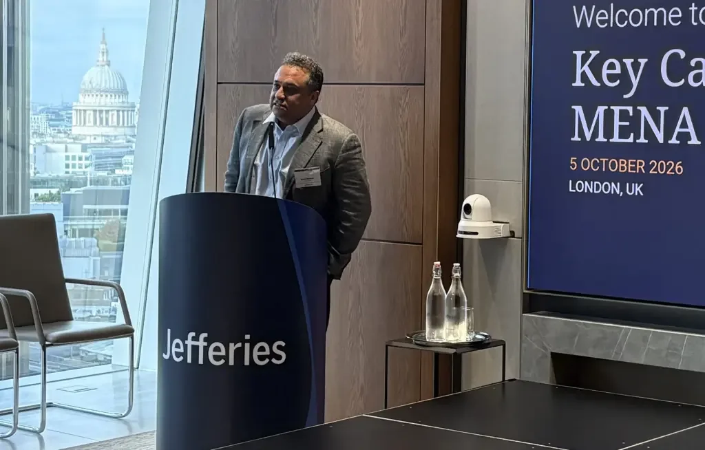 A man speaking at a financial industry conference podium branded Jefferies