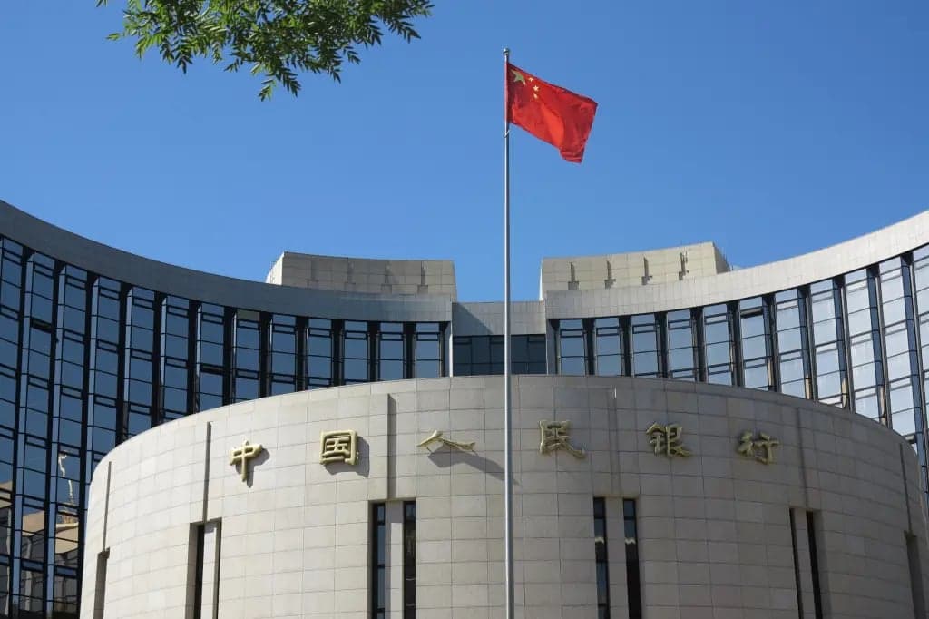 The People's Bank of China headquarters building with a Chinese flag flying in front under a clear blue sky